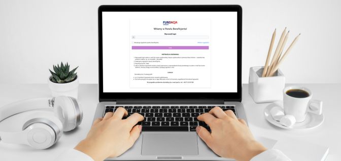 Panel Beneficjenta - Fundacja Votum Dłonie na klawiaturze laptopa, laptop na biurku z otwartą stroną Panelu Beneficjenta, obk na biurku przedmioty biurowe, filiżanka z kawą