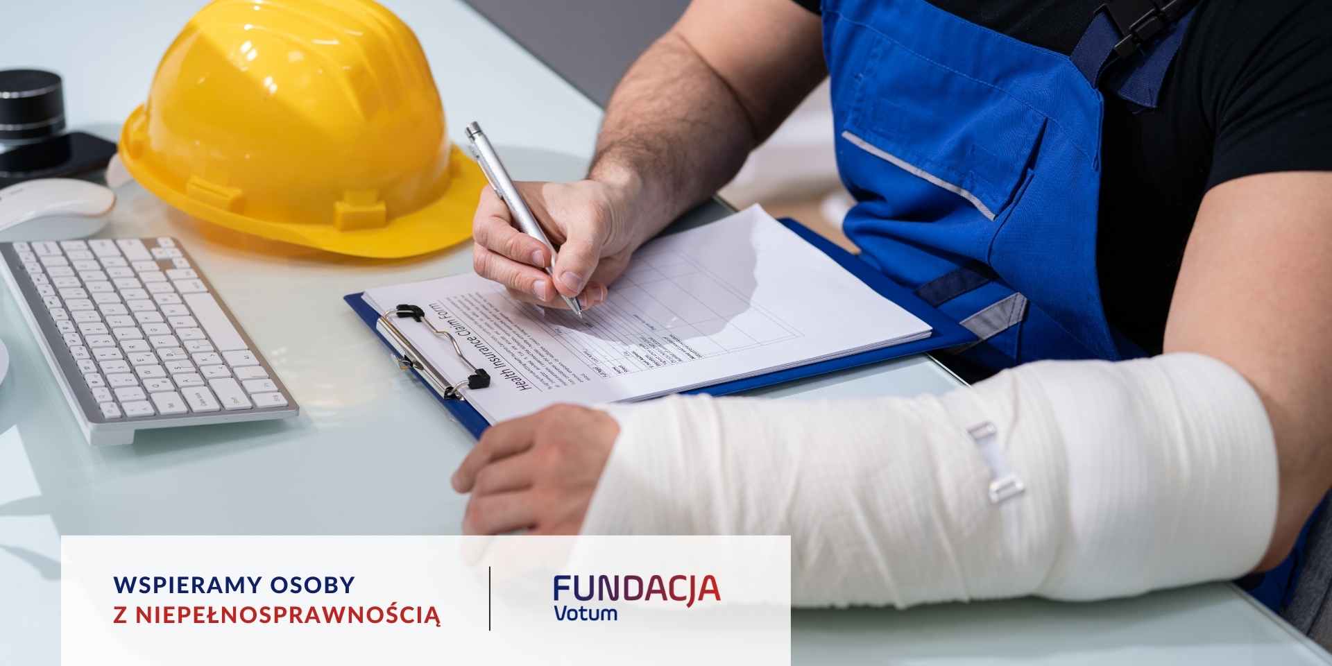 
Mężczyzna w niebieskich ogrodniczkach z zabandażowaną ręką wypełnia formularz odszkodowawczy przy biurku, na którym leży żółty kask ochronny.