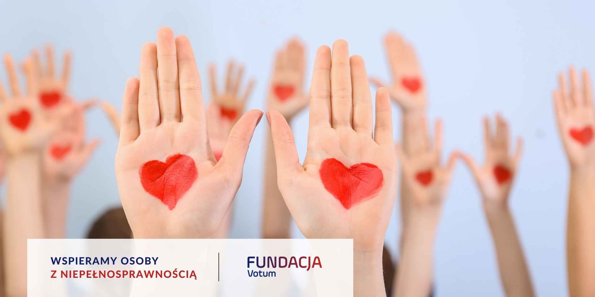 Duża grupa ludzi podnosi dłonie, a na nich namalowane są czerwone serca.